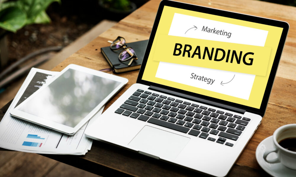 Laptop on a wooden desk displaying the word Branding and the terms Marketing and Strategy