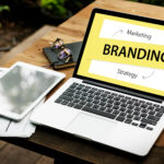 Laptop on a wooden desk displaying the word Branding and the terms Marketing and Strategy