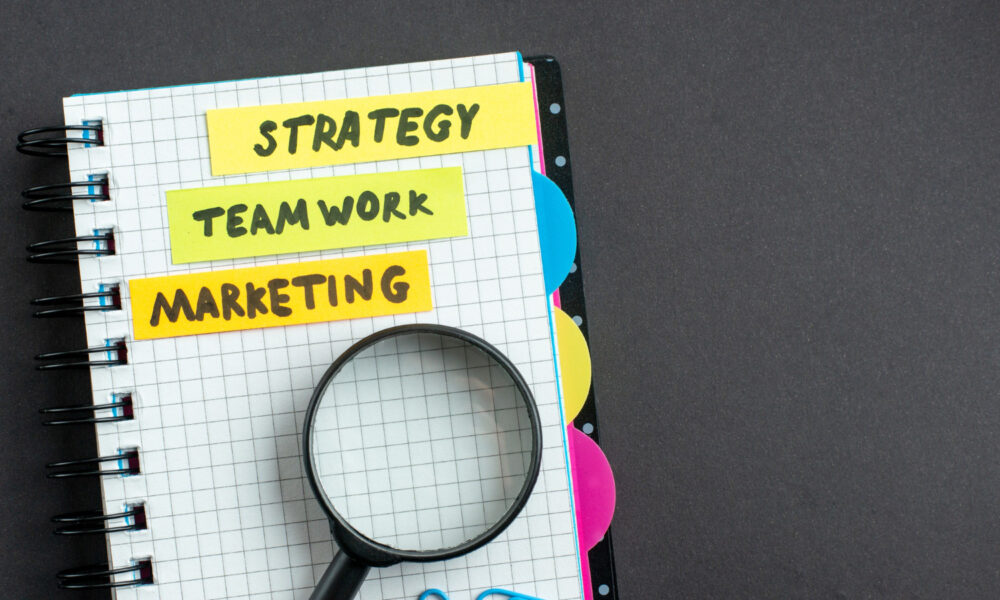 Marketing plan. A notebook with sticky notes labeled “Strategy,” “Teamwork,” and “Marketing.”